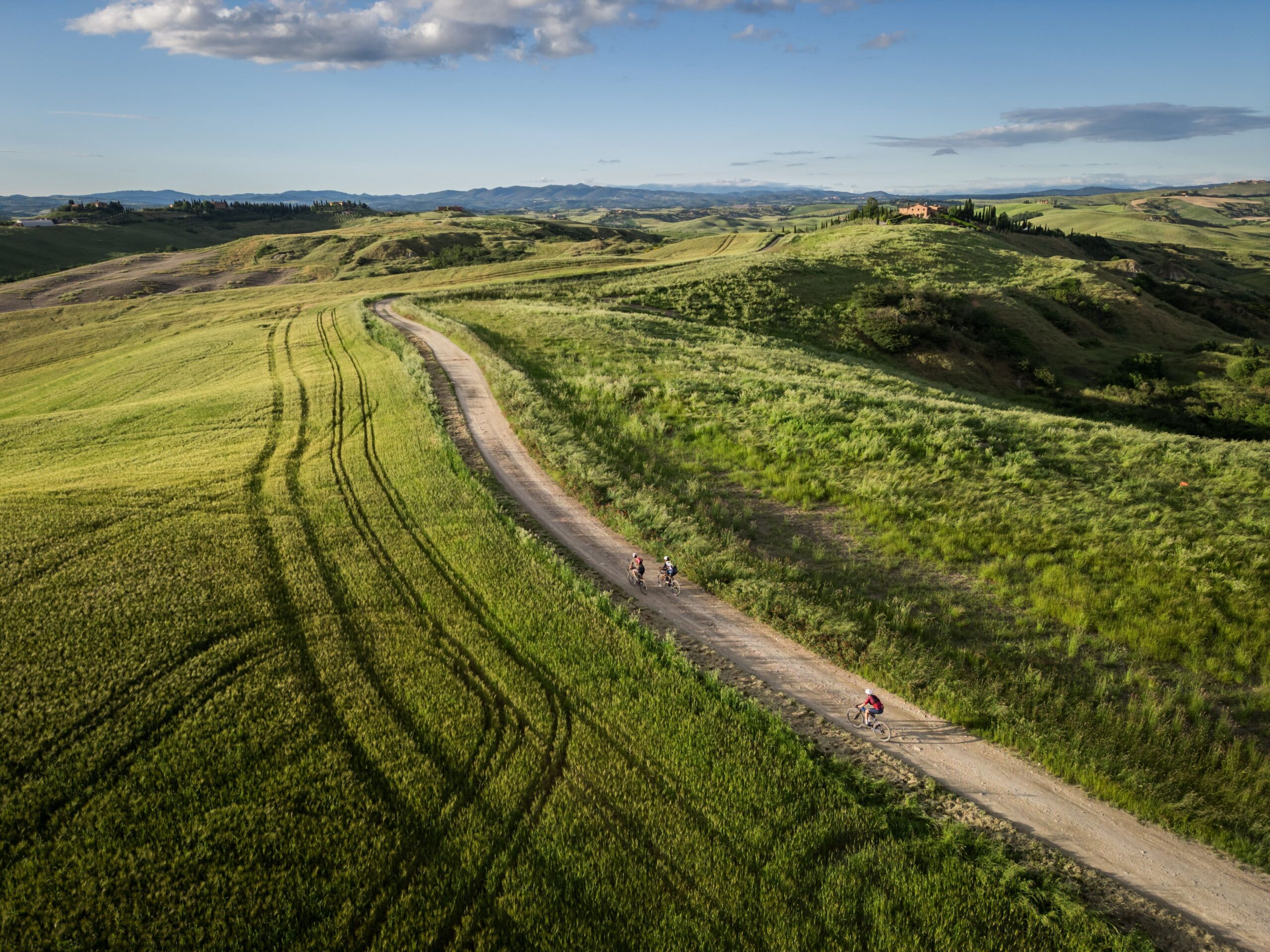 Cyclists riding a white gravel road through green Tuscan hills